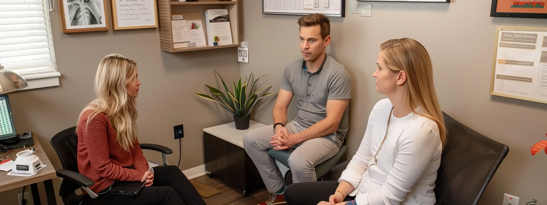 a chiropractor attentively listens to a patient's concerns, surrounded by charts and wellness plans in a cozy office at riverside sports therapy in cochrane.