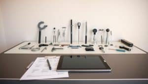A well-lit studio scene showcasing a variety of rehabilitation assessment tools neatly arranged on a sleek, modern desk. In the foreground, a high-quality digital tablet and stylus sit alongside a clipboard with assessment forms. In the middle ground, an array of specialized instruments such as a goniometer, dynamometer, and reflex hammer are meticulously positioned. The background features a neutral, minimalist wall, allowing the tools to take center stage. Soft, directional lighting creates depth and emphasizes the precision and professionalism of the setup, conveying the importance of these assessment tools in the rehabilitation process.