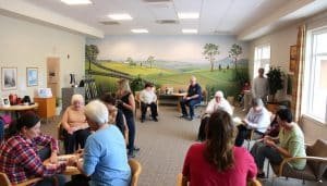 A community-based rehabilitation center in Calgary, with a warm, welcoming atmosphere. In the foreground, a group of people engaged in various therapeutic activities, such as group discussions, physical exercises, and arts and crafts. The middle ground features a bright, open-plan space with natural lighting, comfortable seating, and therapeutic equipment. In the background, a mural depicting scenes of nature and community, conveying a sense of tranquility and connection. The overall mood is one of support, empowerment, and a focus on holistic well-being. The image is captured with a wide-angle lens, emphasizing the collaborative and inclusive nature of the programs.